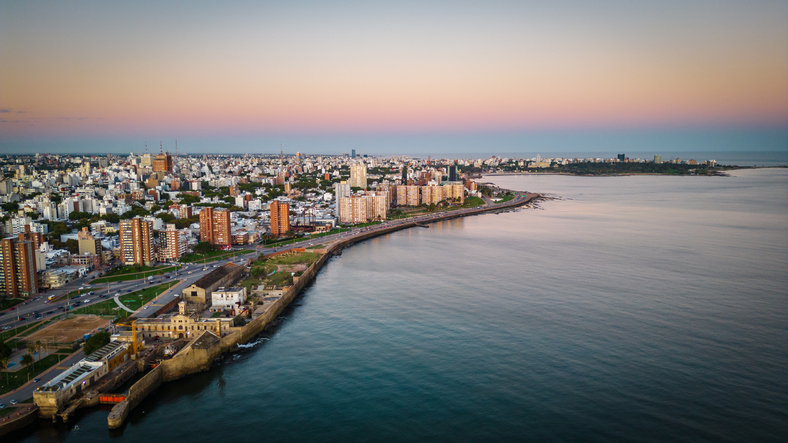 Luftaufnahme der beleuchteten Küstenstraße und Skyline von Montevideo während des Sonnenuntergangs.