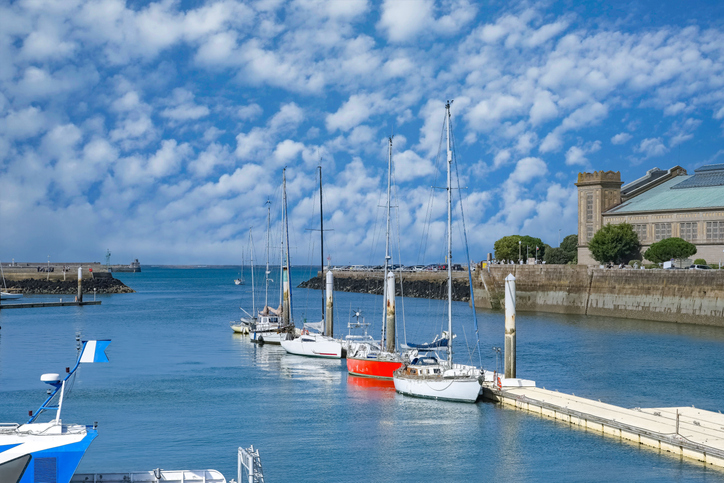 Mehrere Segelboote liegen friedlich an einem Steg im Hafen von Cherbourg unter einem dramatischen Wolkenhimmel.