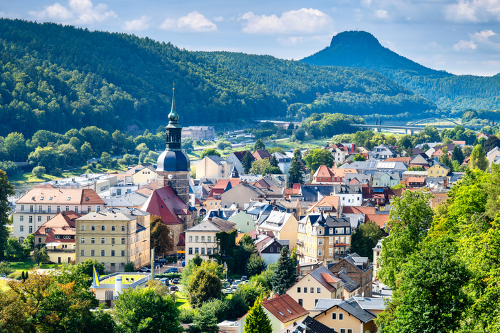Eine kleine Stadt liegt zwischen grünen Hügeln und markanten Felsen der Sächsischen Schweiz.