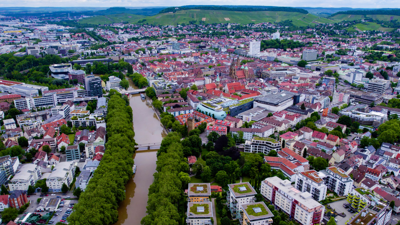Ein weiter Blick aus der Vogelperspektive auf das Stadtgebiet von Heilbronn mit dem Neckar als zentraler Achse, umgeben von Weinbergen.