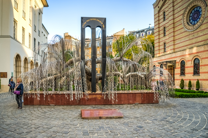 Das metallene Lebensbaum-Mahnmal steht in einem Innenhof neben historischen Gebäuden in Budapest.