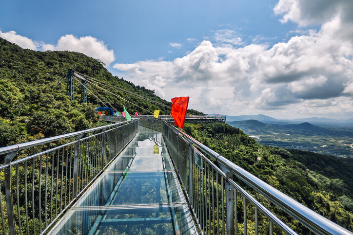 Ein gläserner Pfad mit roten Fahnen führt entlang eines bewaldeten Bergrückens in Hainan und bietet einen weiten Blick über das Tal.