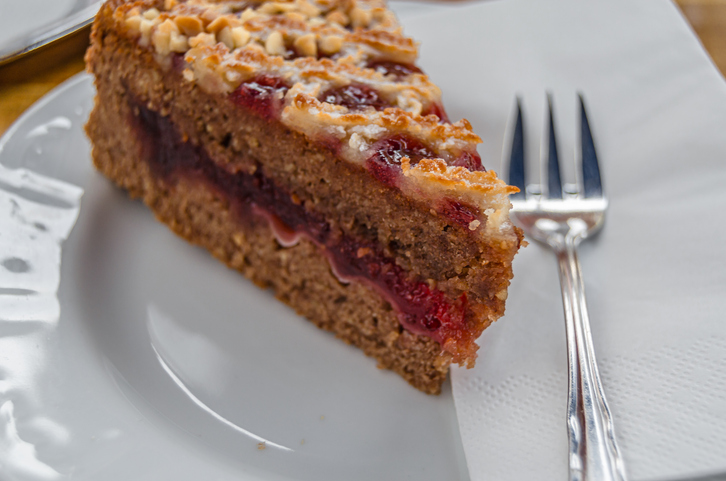 Ein einzelnes Stück einer traditionellen Linzer Torte liegt auf einem weißen Teller neben einer silbernen Kuchengabel.