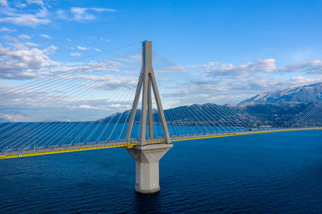 Eine große Schrägseilbrücke überspannt das tiefblaue Meer mit Bergen im Hintergrund.