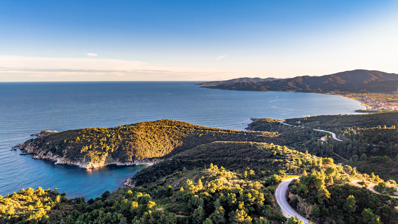 Ein weites Panorama der Küstenlinie von Sarti bei warmem Licht, das sanft über die Hügel und das Wasser fällt.