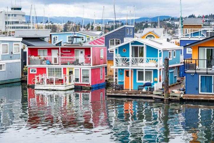 Farbenfrohe Hausboote spiegeln sich im Wasser am Hafen von Victoria in Kanada.