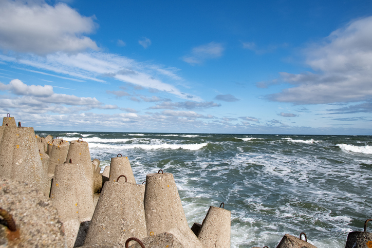 Massive Beton-Wellenschutzblöcke säumen die Küste von Kolberg, während sich dahinter die stürmische Ostsee unter einem bewölkten Himmel auftürmt.