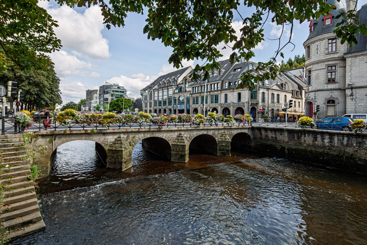 Eine steinerne Brücke, geschmückt mit Blumenkästen, spannt sich über den Fluss Odet, im Hintergrund sind städtische Gebäude zu sehen