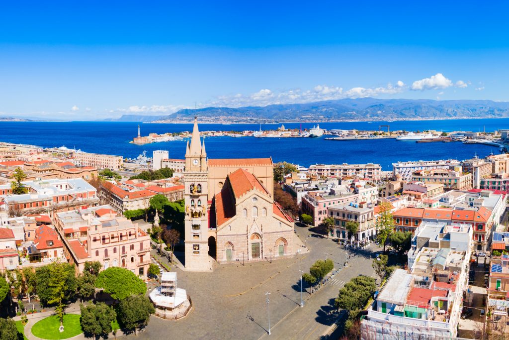 Luftaufnahme der Kathedrale von Messina mit ihrem markanten Glockenturm vor dem Hafenbecken