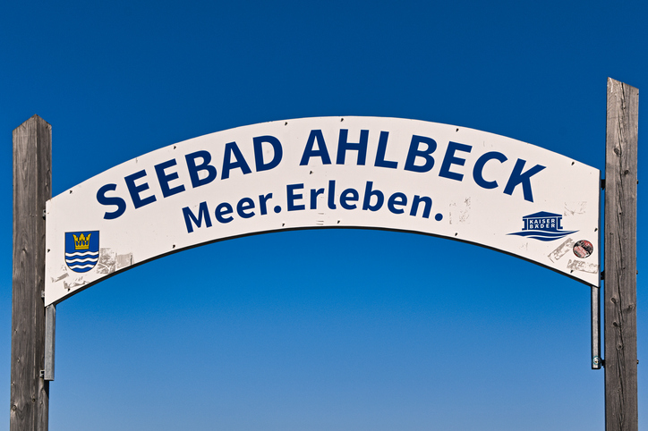 Ein großes Schild mit der Aufschrift „Seebad Ahlbeck – Meer.Erleben.“ unter blauem Himmel.