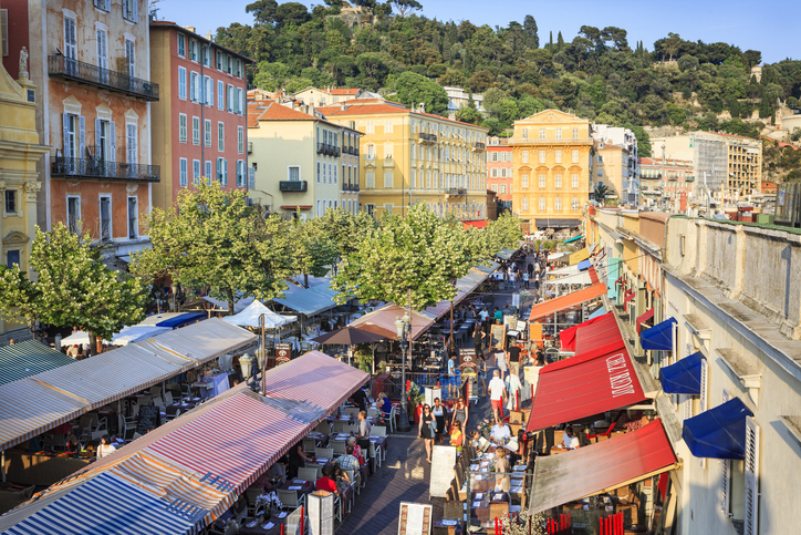 Bunte Marktstände und historische Häuser prägen eine belebte Gasse in Nizza.