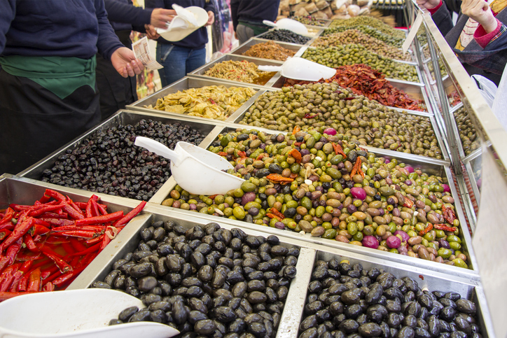 Verschiedene Sorten eingelegter Oliven und Peperoni in großen Metallbehältern auf einem Markt in Syrakus.