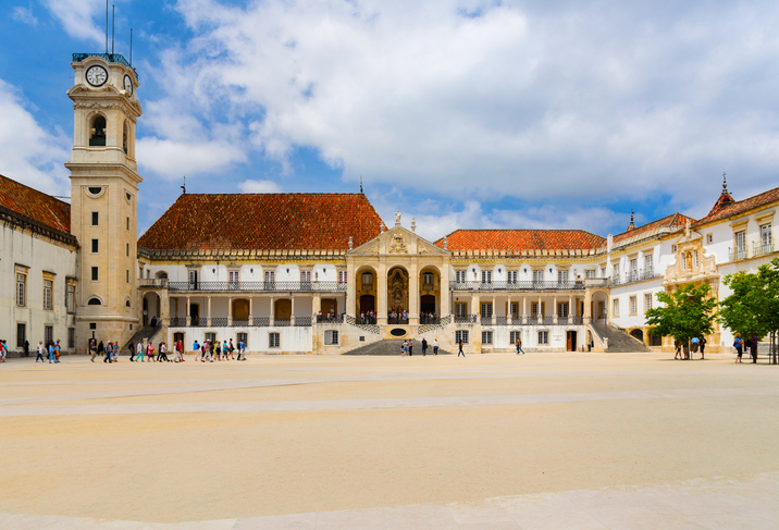 Besucher schlendern über den weitläufigen, hellen Innenhof der historischen Universität Coimbra mit ihrem markanten Glockenturm.