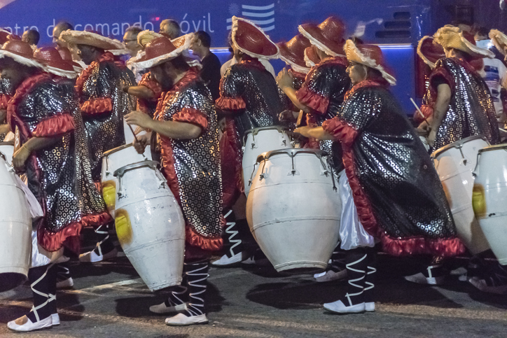 Performer in glitzernden Kostümen und mit großen Trommeln bei einer Karnevalsparade in Montevideo.