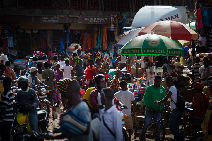Ein belebter, farbenfroher Markt in einer Stadt in Sierra Leone, auf dem Menschen zwischen Warenständen und Motorrädern interagieren.
