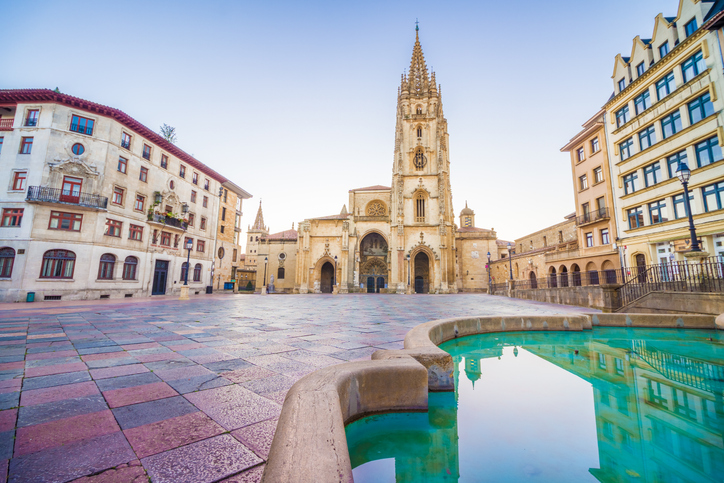 Die Kathedrale von Oviedo steht an einem hellen Platz mit Wasserbecken im Vordergrund.
