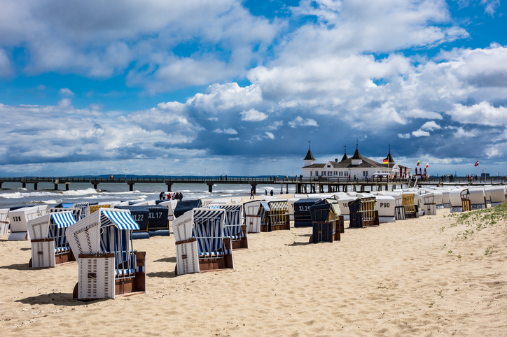 Strandkörbe im Vordergrund mit der ikonischen Seebrücke von Ahlbeck im Hintergrund unter wolkigem Himmel.