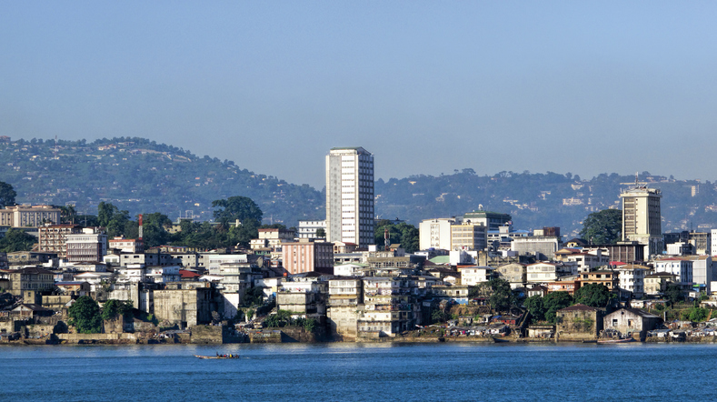Eine weite Ansicht der Küstenstadt Freetown in Sierra Leone mit einer Mischung aus modernen Gebäuden und dichten grünen Bergen im Hintergrund.