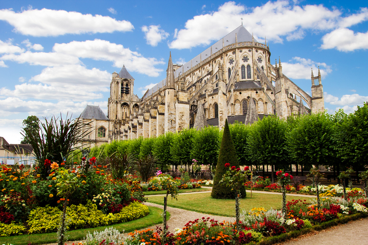 Eine prächtige Gartenanlage mit blühenden Blumenbeeten direkt vor der massiven Außenwand der Kathedrale von Bourges.