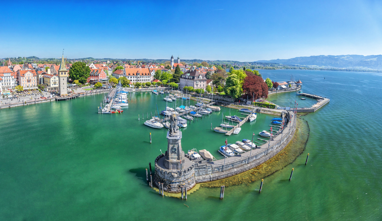 Weitwinkelansicht der gesamten Hafeneinfahrt mit dem Löwen, dem Leuchtturm und den im Wasser liegenden Booten bei strahlendem Sonnenschein