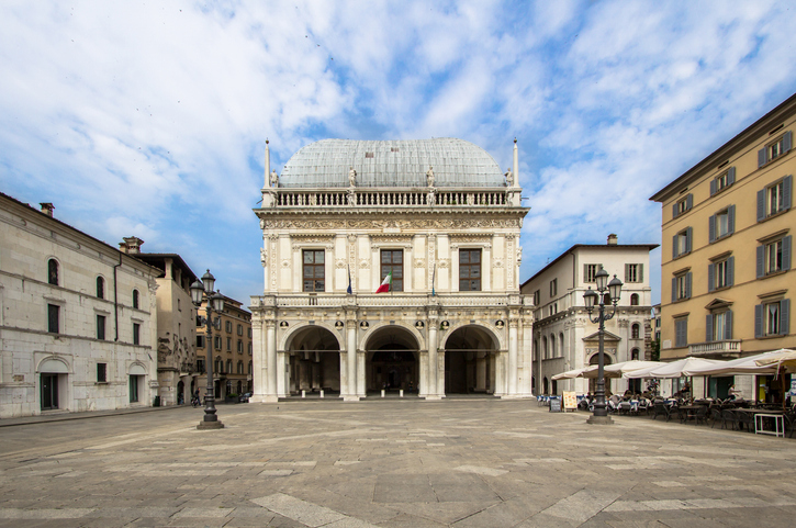 Der historische Platz Piazza della Loggia mit dem prachtvollen Palazzo della Loggia im Hintergrund unter blauem Himmel.