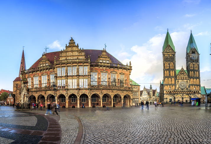 Eine weite Ansicht des prächtigen Rathauses und der hohen Doppeltürme des St.-Petri-Doms unter einem hellblauen Himmel.