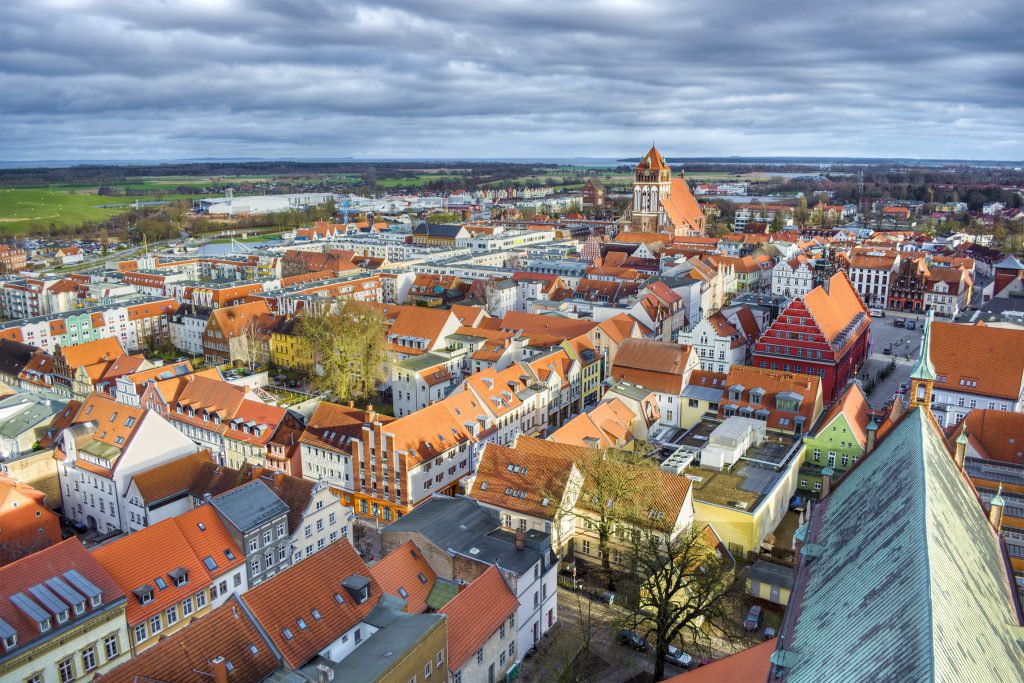 Eine Luftaufnahme zeigt die dichte, rote Ziegeldachlandschaft der Greifswalder Altstadt mit ihren markanten Kirchtürmen.