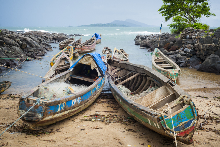 Mehrere hölzerne, bunt bemalte Fischerboote liegen an einem felsigen Küstenabschnitt in Sierra Leone im Wasser.