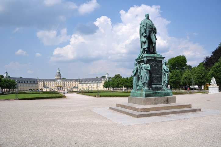 Eine große Bronzestatue steht auf dem weiten Platz vor dem Karlsruher Schloss.