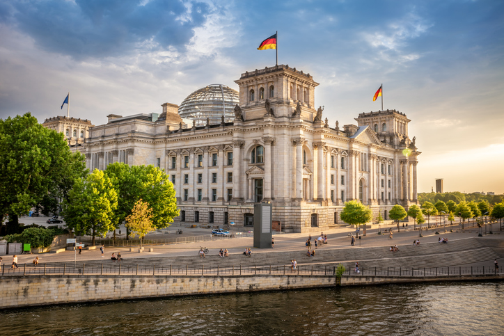 Das Reichstagsgebäude mit Glaskuppel steht am Spreeufer im warmen Abendlicht.