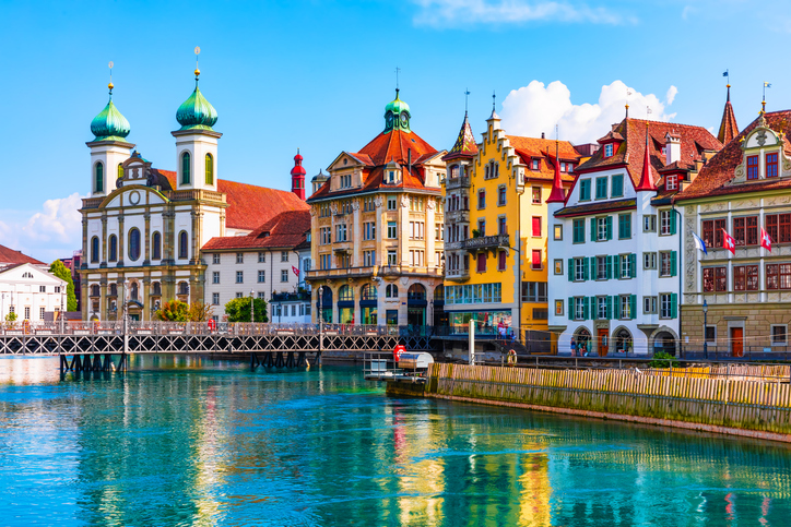 Die Jesuitenkirche und farbige Altstadthäuser spiegeln sich im Wasser der Reuss in Luzern.