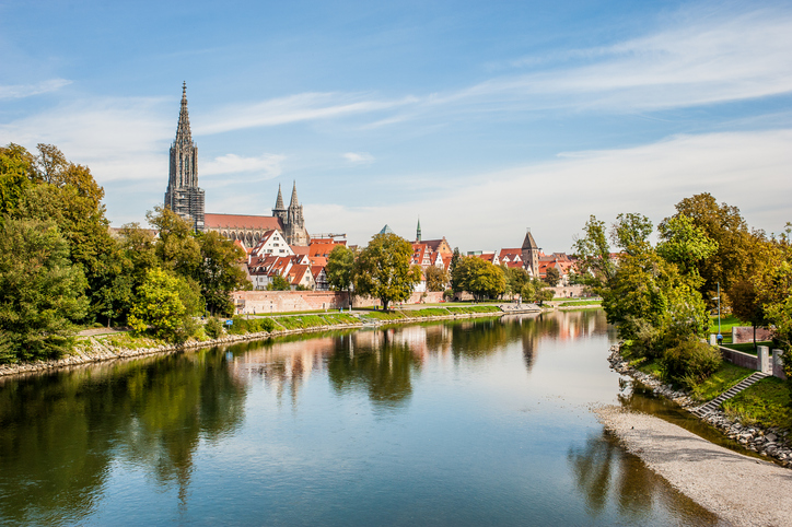 Ruhiger Fluss in Ulm mit Blick auf das Ufer, Bäume und das Ulmer Münster im Hintergrund.