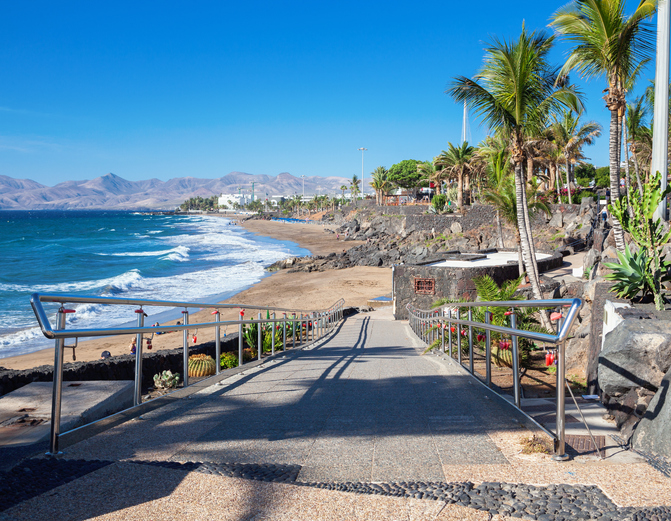 Eine Treppe führt zu einer Strandpromenade mit Palmen, Meer und Küste auf Lanzarote.