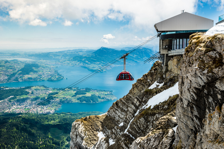 Eine rote Seilbahn fährt am Pilatus über Felsen mit Blick auf Luzern und den Vierwaldstättersee.