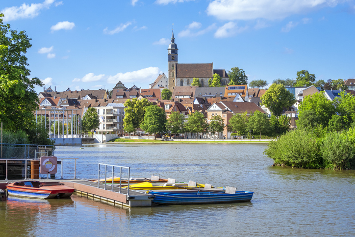 See in Böblingen mit kleinen Booten, Steg, grünen Ufern und Stadtansicht im Hintergrund.