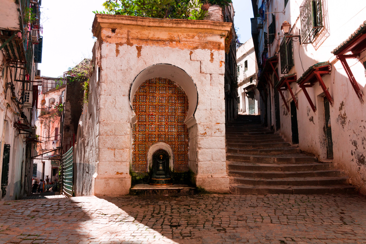 Ein alter Brunnen mit Fliesen liegt zwischen Treppen und engen Gassen in der Kasbah von Algier.