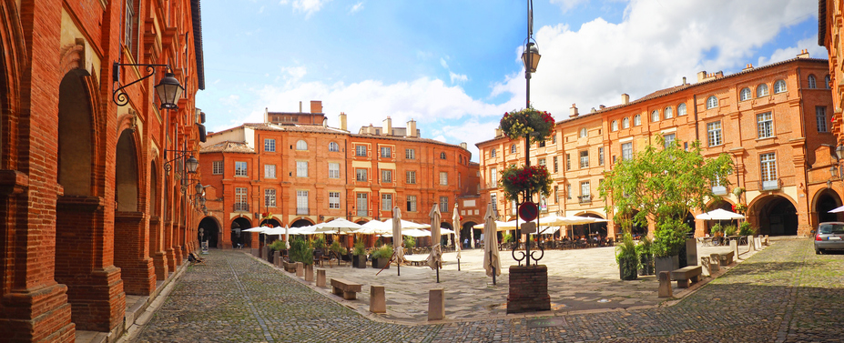 Historischer Platz mit roten Backsteinarkaden, Cafés und Sonnenschirmen in Montauban.