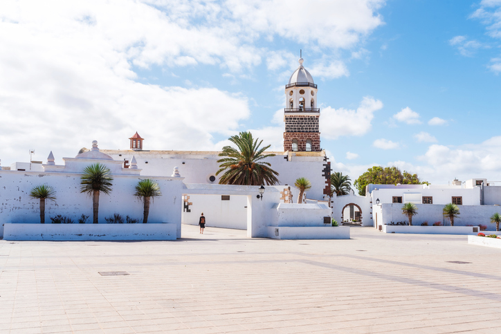 Ein heller Platz mit weißer Kirche, Palmen und blauem Himmel in einem Ort auf Lanzarote.