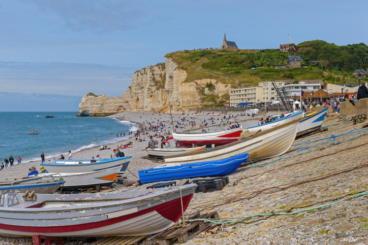 Boote liegen am Kiesstrand von Étretat vor hohen Kreidefelsen nahe Le Havre.