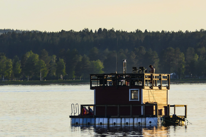 Kleine schwimmende Sauna oder Badeplattform auf einem ruhigen See bei Luleå im Abendlicht.