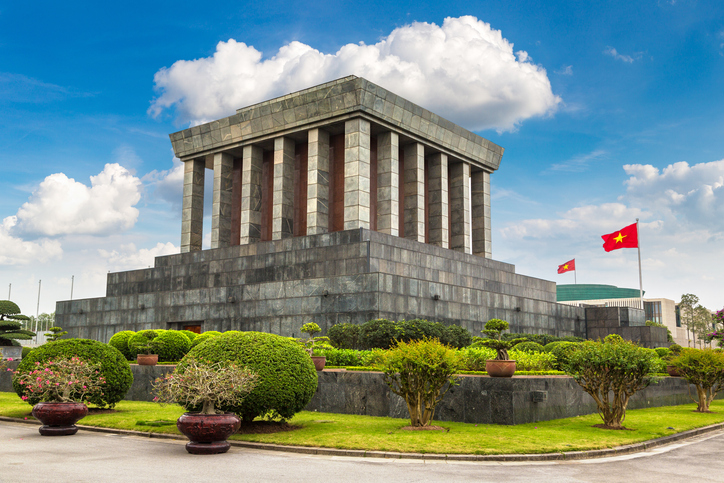 Das Ho-Chi-Minh-Mausoleum in Hanoi steht vor einer gepflegten Grünanlage unter blauem Himmel.