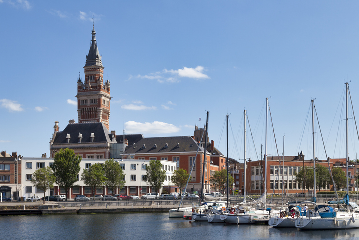 Segelboote liegen im Hafen, dahinter steht das Rathaus von Dunkerque.