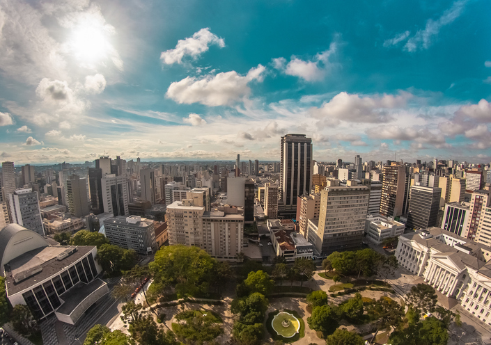 Blick über die Skyline von Curitiba mit Hochhäusern, Parkflächen und weitem Himmel.