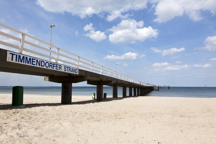 Seebrücke von Timmendorfer Strand mit Schriftzug und sandigem Strand unter blauem Himmel.