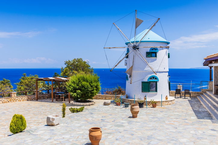 Weiße Windmühle mit blauem Dach auf einer steinernen Terrasse mit Meerblick auf Zakinthos