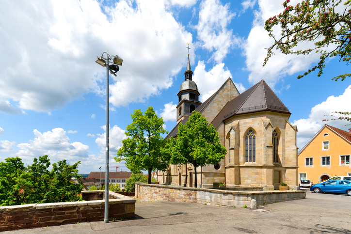 Historische Kirche in Böblingen mit Steinmauern, Bäumen und blauem Himmel.