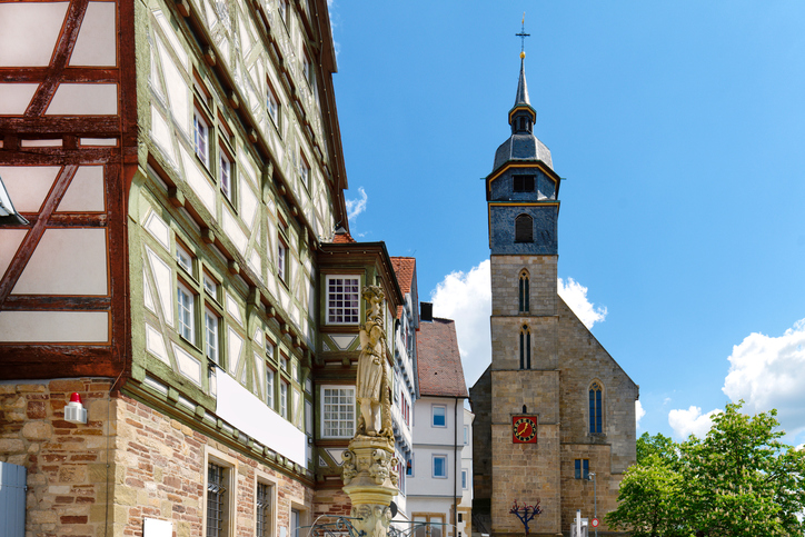 Altstadt von Böblingen mit Fachwerkhaus, Brunnenfigur und Kirchturm unter blauem Himmel.