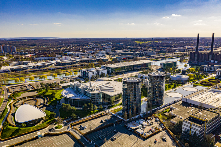 Blick auf die Autostadt Wolfsburg mit modernen Gebäuden, Wasserflächen, Parkanlagen und Volkswagenwerk im Hintergrund.