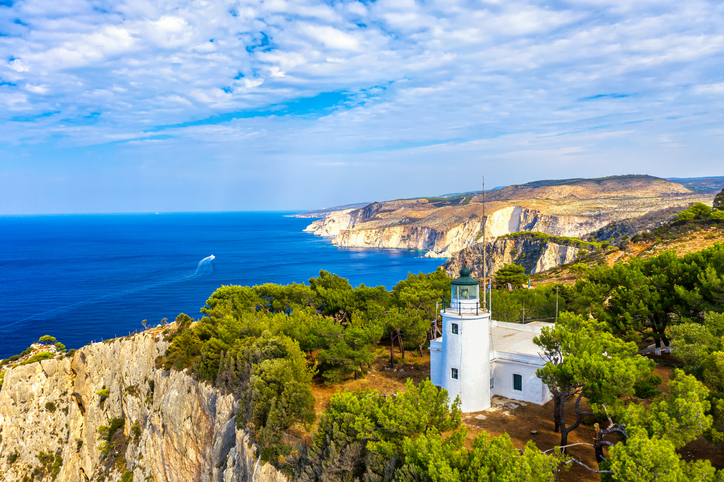 Weißer Leuchtturm auf einer bewaldeten Klippe mit weitem Blick auf das Meer auf Zakinthos