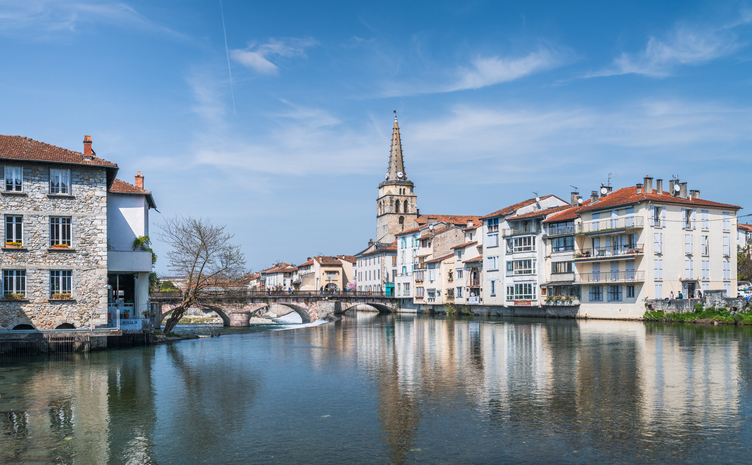 Fluss mit Spiegelung, Steinbrücke und Kirchturm in Saint-Girons unter blauem Himmel